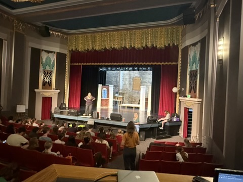 A Singin' in the Rain rehearsal with a projected city-wall setting behind the stage.