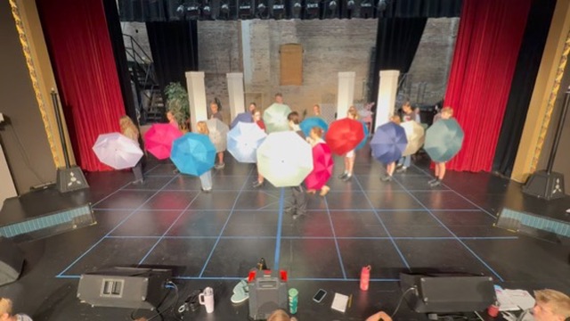 Performers rehearsing Singin' in the Rain choreography with colorful umbrellas.
